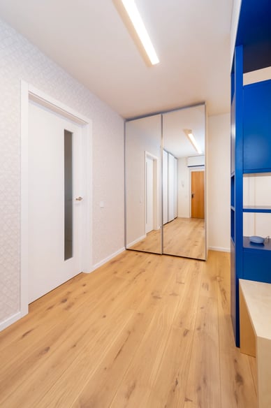 Světlé dřevo, zrcadlová skříň a modrý nábytek v moderní chodbě.